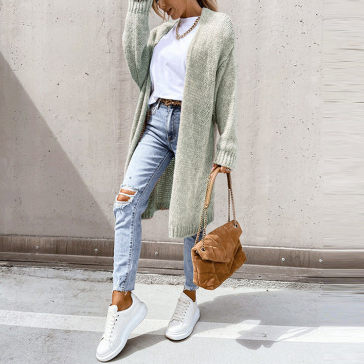 Frau in grauem Strickcardigan, weißem T-Shirt, zerrissenen Jeans, weißen Sneakers, brauner Tasche.