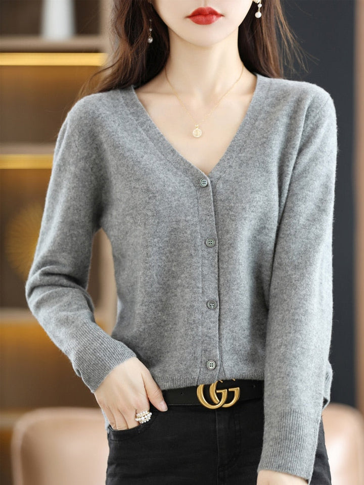 Frau trägt grauen V-Ausschnitt-Cardigan, schwarze Hose, goldene Gürtelschnalle, eleganter Look.