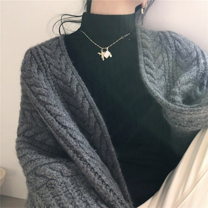 Frau in grauem Strickcardigan und schwarzem Rollkragenpullover, modisch, gemütlich.