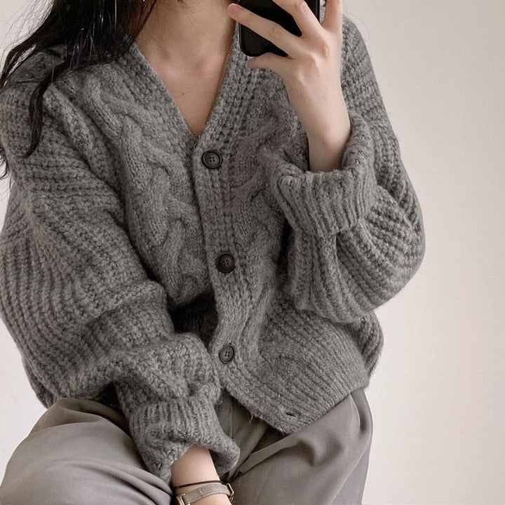 Frau trägt graue Strickjacke mit Zopfmuster, V-Ausschnitt und Knöpfen, gemütlicher Winterlook.