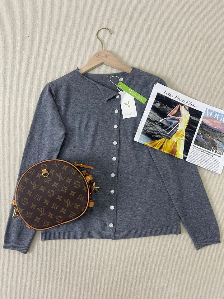 Grauer Cardigan mit Knöpfen, Louis Vuitton Tasche, Vogue-Magazin auf beigem Hintergrund.