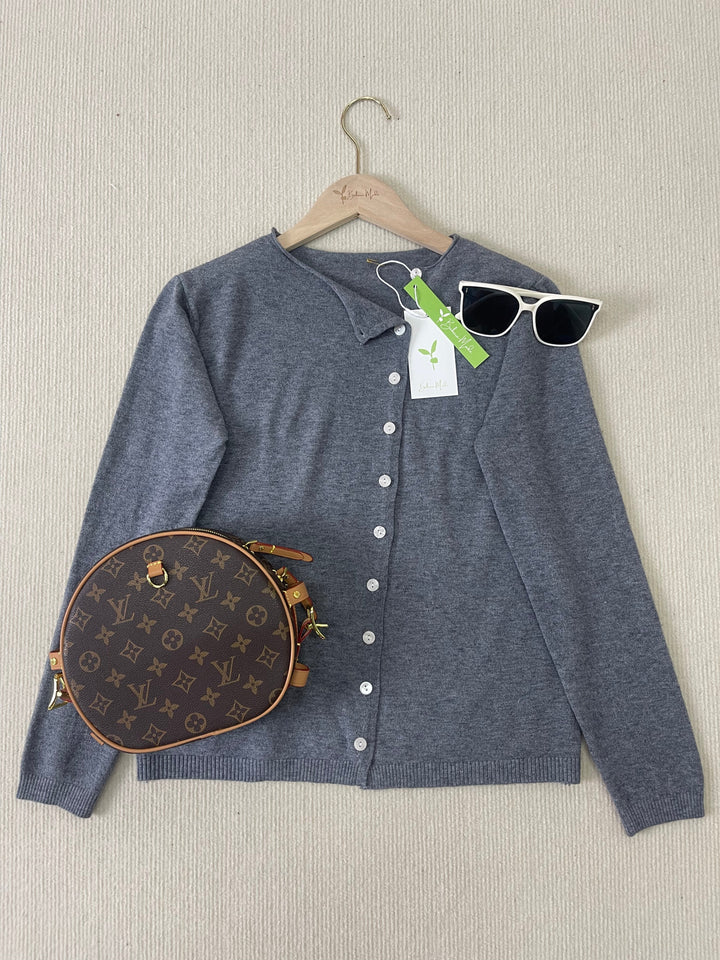 Grauer Cardigan mit weißen Knöpfen, Louis Vuitton Tasche, weiße Sonnenbrille auf beigem Hintergrund.