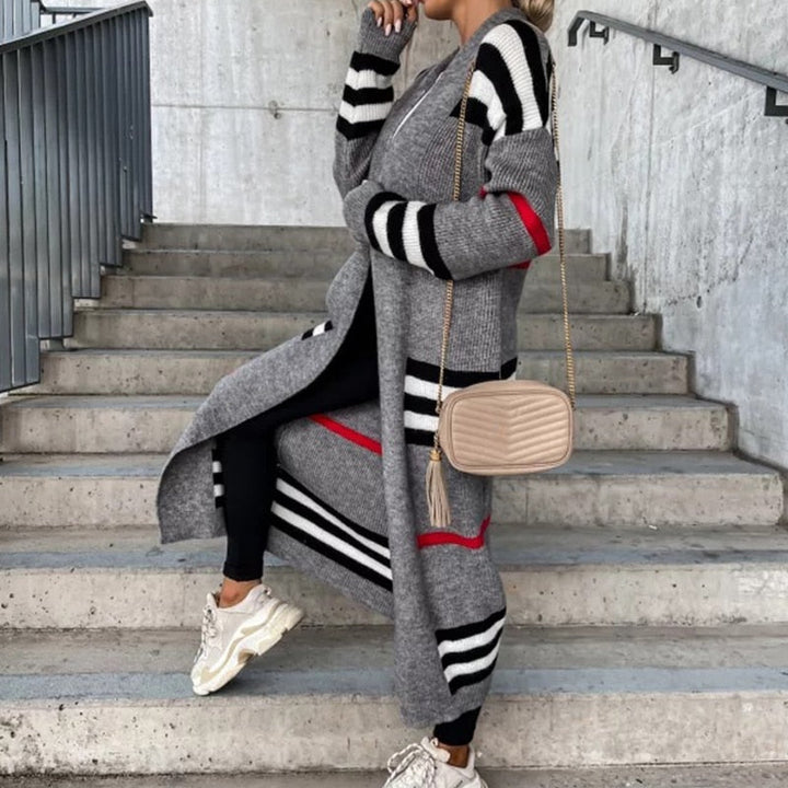 Frau in grauem gestreiftem Strickmantel, schwarze Leggings, weiße Sneaker, beige Umhängetasche.