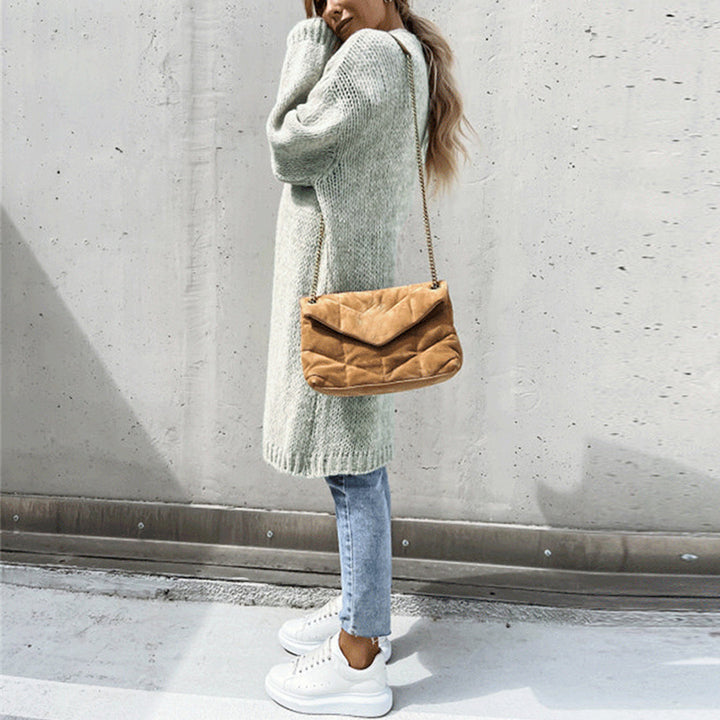 Frau in grauem Strickkleid, blauer Jeans, weißen Sneakers, braune Umhängetasche, urbaner Hintergrund.