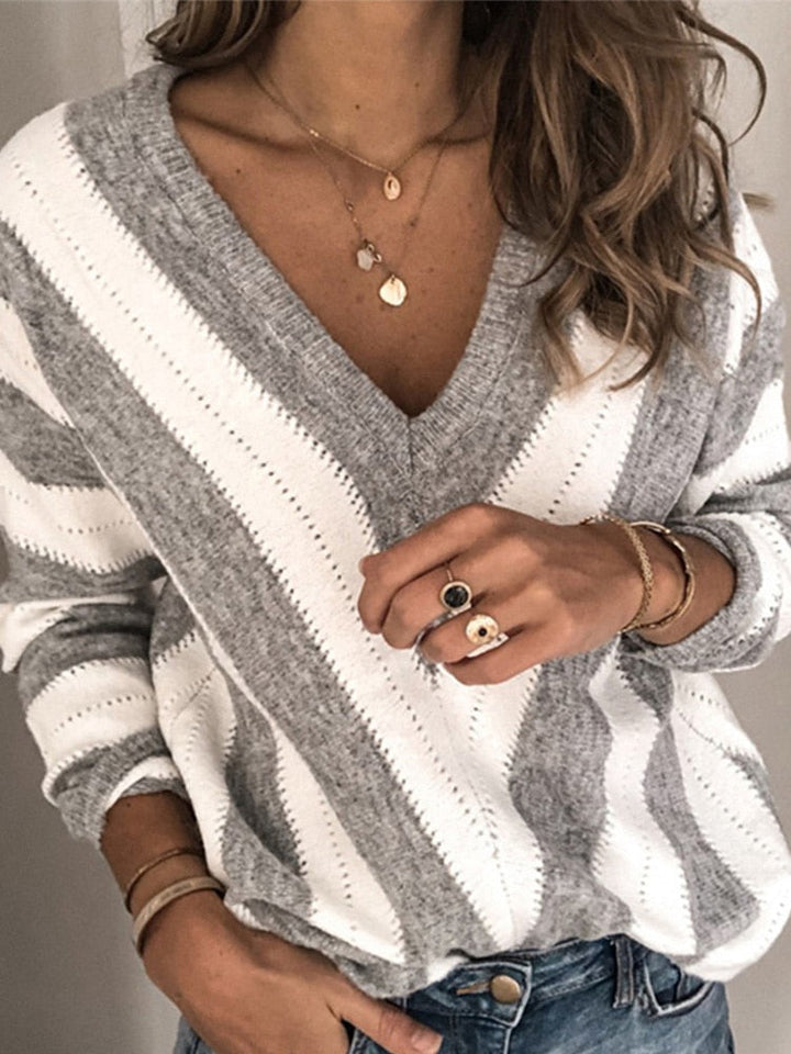 Frau trägt grauen gestreiften Pullover, V-Ausschnitt, Schmuck, lässiger Stil.