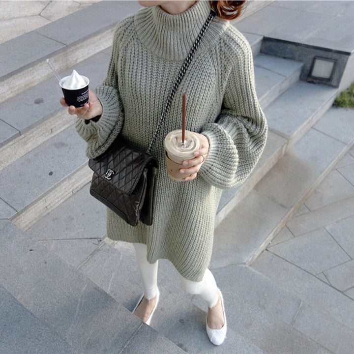 Frau in grauem Strickpullover, hält Kaffee und Eis, trägt schwarze Umhängetasche, weiße Hose.
