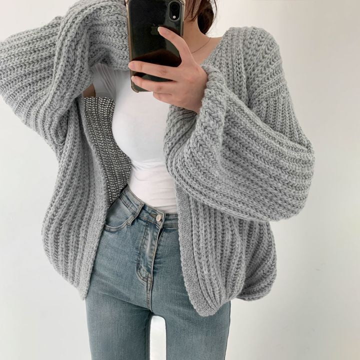 Frau in grauem Strickpullover, weiße Bluse, blaue Jeans, Smartphone, modisch, gemütlich.