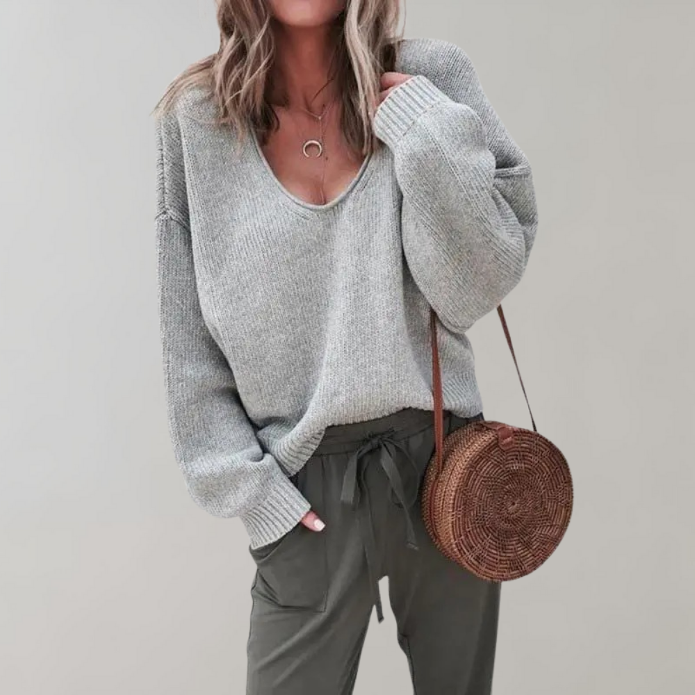 Frau in grauem Strickpullover mit runder Strohtasche und olivgrüner Hose.