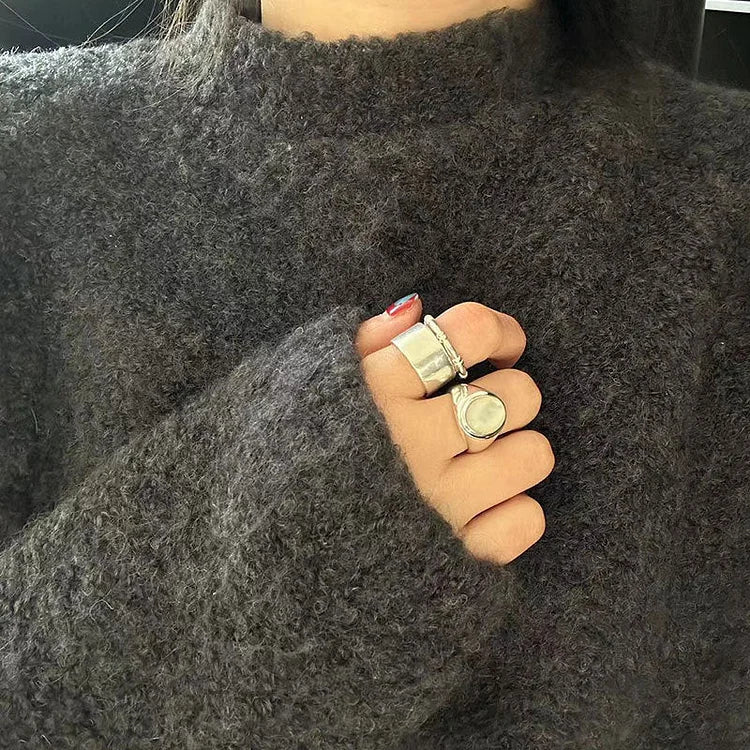 Dunkelgrauer Strickpullover aus Wolle, Hand mit silbernen Ringen, gemütliche Wintermode.