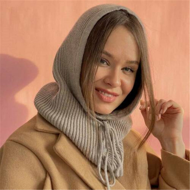 Frau mit grauem Strickschal und Kapuze, beige Mantel, lächelnd, modisches Winteroutfit.
