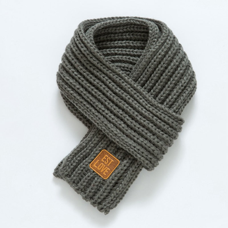Grauer Strickschal aus Wolle mit Lederetikett, modisches Accessoire für kalte Tage.