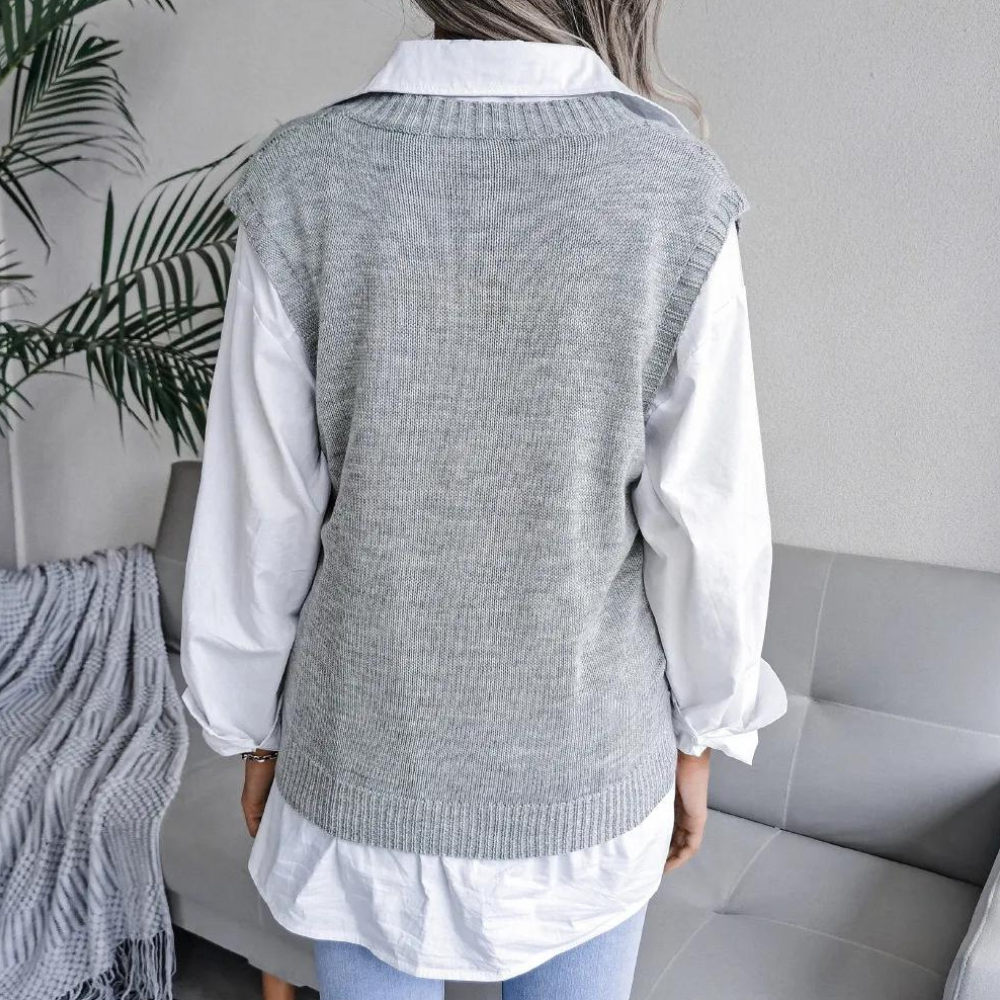 Frau in grauem Strickpullunder über weißer Bluse, moderne Mode, gemütliches Wohnzimmer.