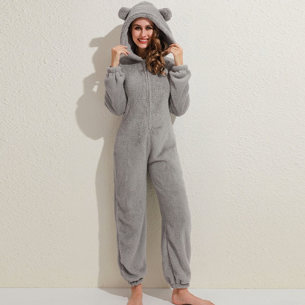 Frau in grauem Plüsch-Onesie mit Kapuze und Bärenohren, gemütliche Hausbekleidung.