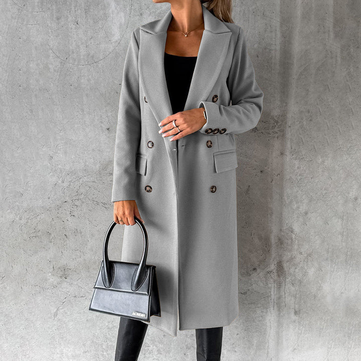 Frau in grauem Wintermantel mit schwarzer Handtasche vor grauem Hintergrund.