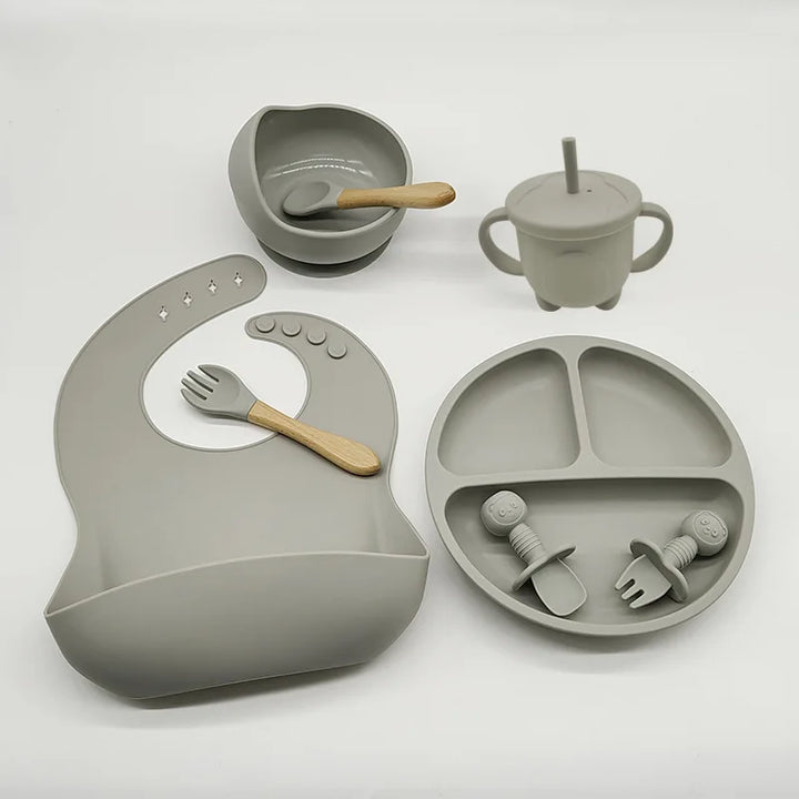 Graues Silikon-Babygeschirr-Set mit Lätzchen, Teller, Schüssel, Becher und Besteck.