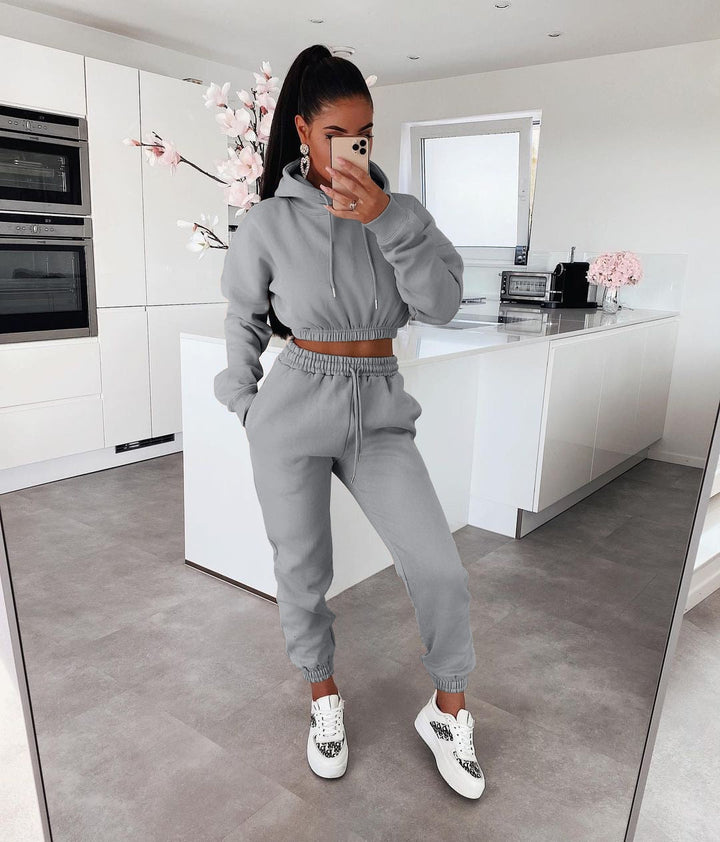 Frau in grauem Jogginganzug in moderner Küche, trägt weiße Sneaker, macht Selfie.
