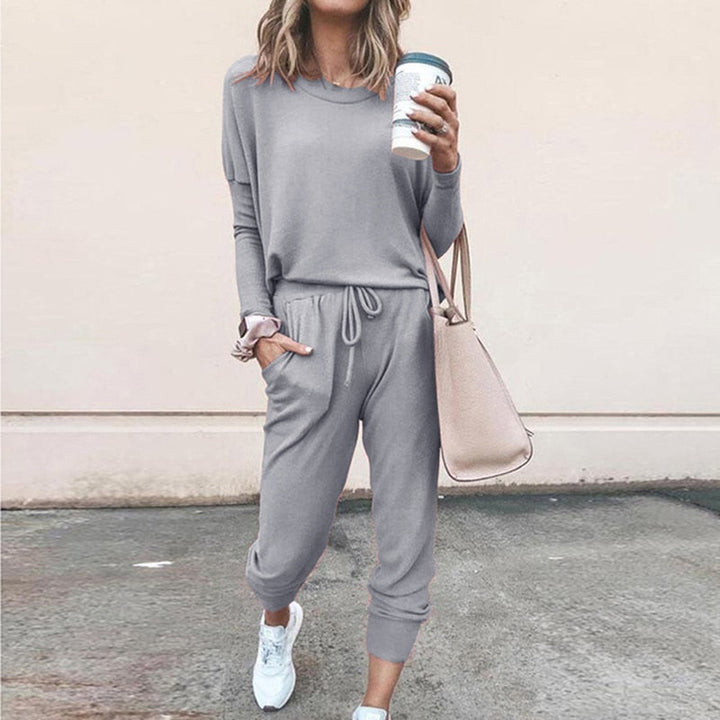 Frau in grauem Jogginganzug mit Kaffeebecher und beiger Tasche, lässige Mode.