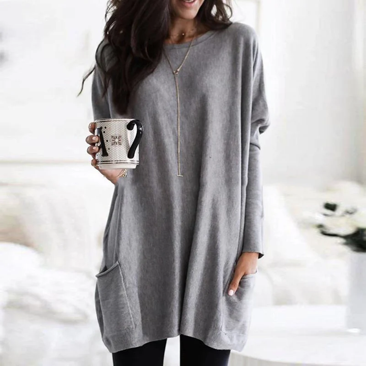 Frau in grauem Oversize-Pullover mit Tasse, gemütliche Mode, lässiger Stil, Wohnzimmer.