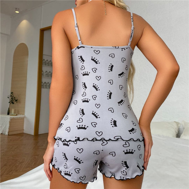 Frau in grauem Pyjama-Set mit Kronen- und Herzmuster, Schlafzimmer-Hintergrund.