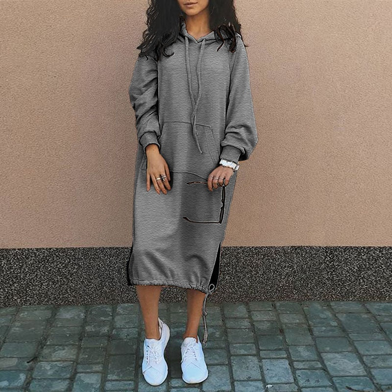 Frau in grauem Kapuzenkleid, lässig, mit weißen Sneakers, modisch, urbaner Stil.