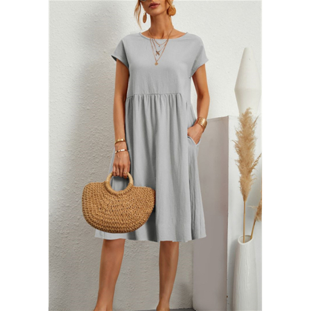 Frau in grauem Baumwoll-Leinen-Kleid, Boho-Stil, mit Strohtasche, Sommermode.