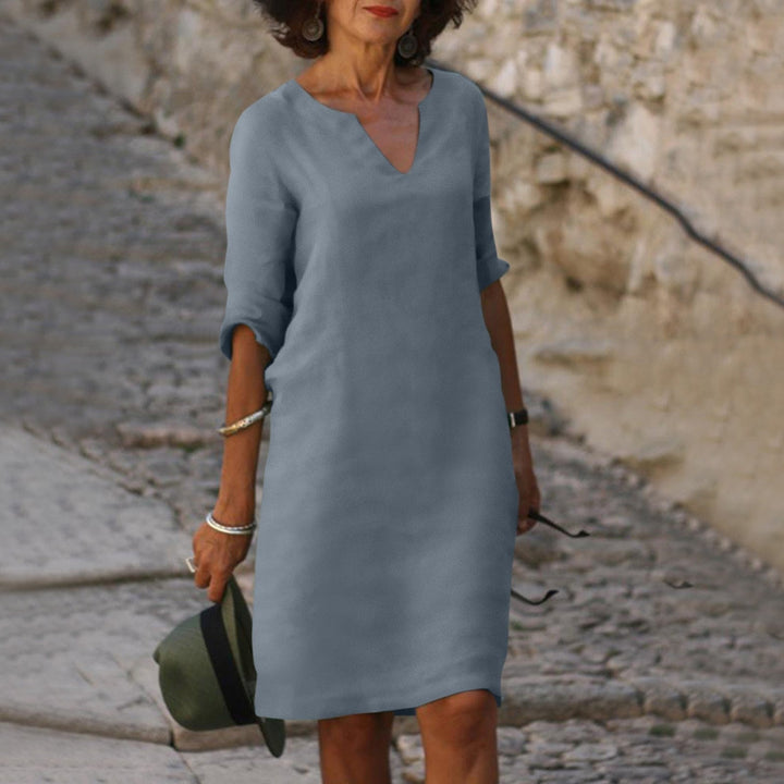 Frau in grauem Leinenkleid mit V-Ausschnitt, Sommermode, lässig, elegant, draußen.