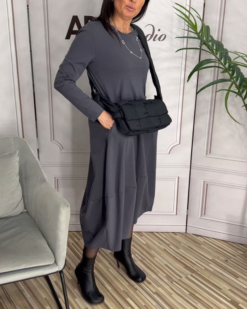 Frau in grauem Kleid mit schwarzer Umhängetasche und Stiefeln, moderne Mode, Innenraum.