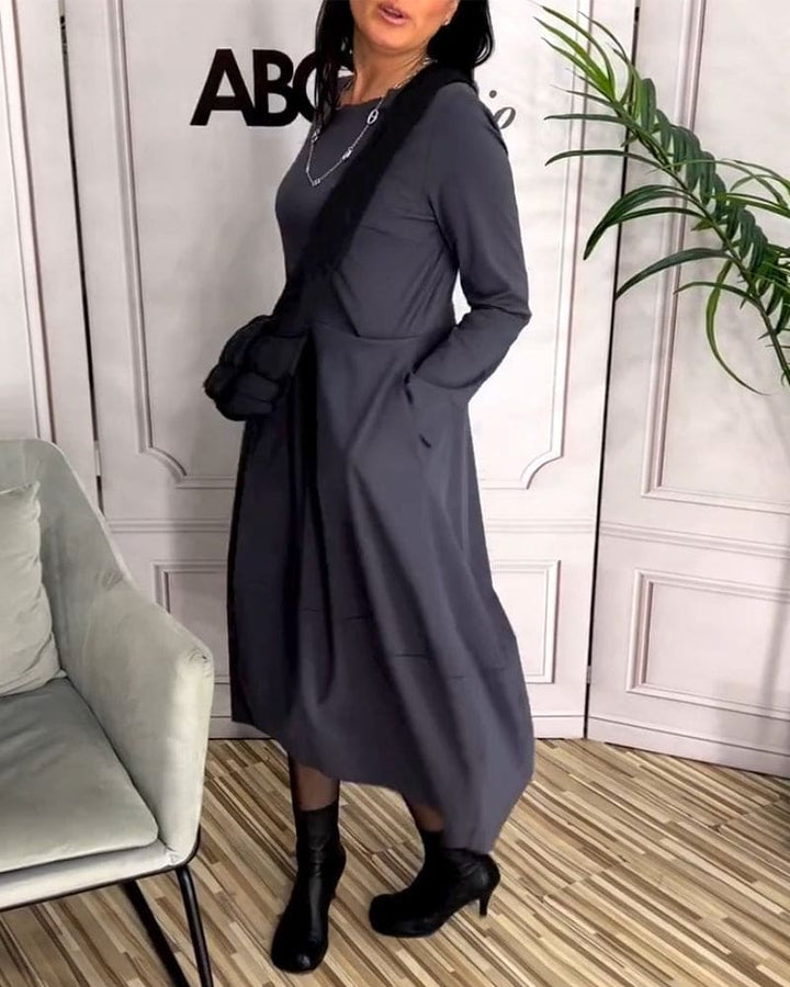 Frau in grauem Maxikleid mit schwarzer Umhängetasche und Stiefeln, moderne Mode, Innenraum.