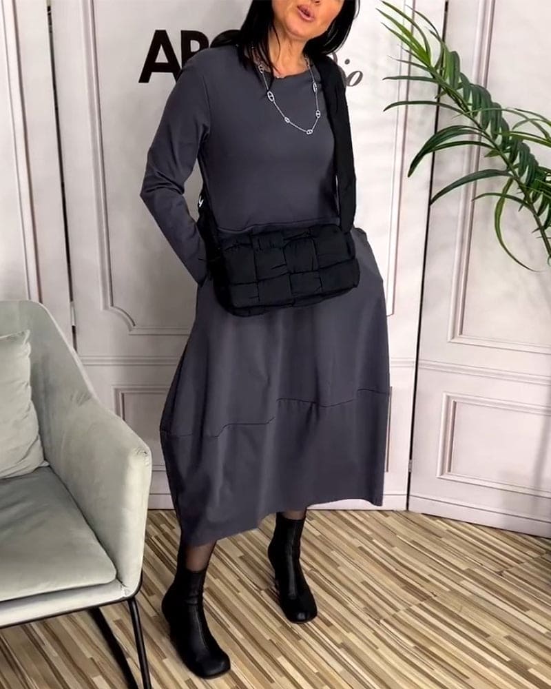 Frau in grauem Kleid mit schwarzer Umhängetasche und Stiefeln, moderne Mode, Innenraum.