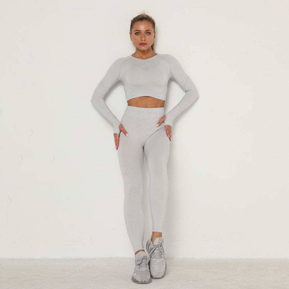 Frau in grauem nahtlosem Sport-Set, Langarm-Top und Leggings, Fitnessmode, Studioaufnahme.