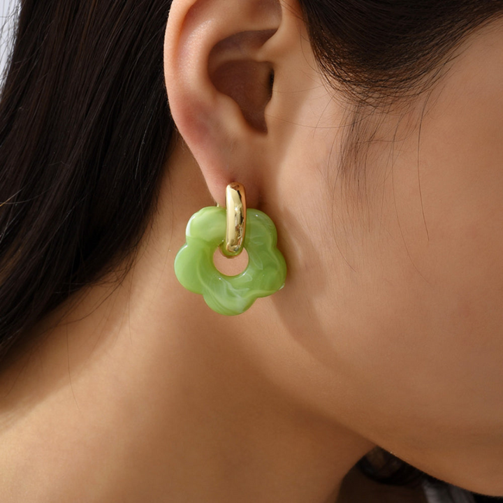 Grüner Blumen-Ohrring aus Harz und Gold an Ohr, modisches Accessoire, Nahaufnahme.