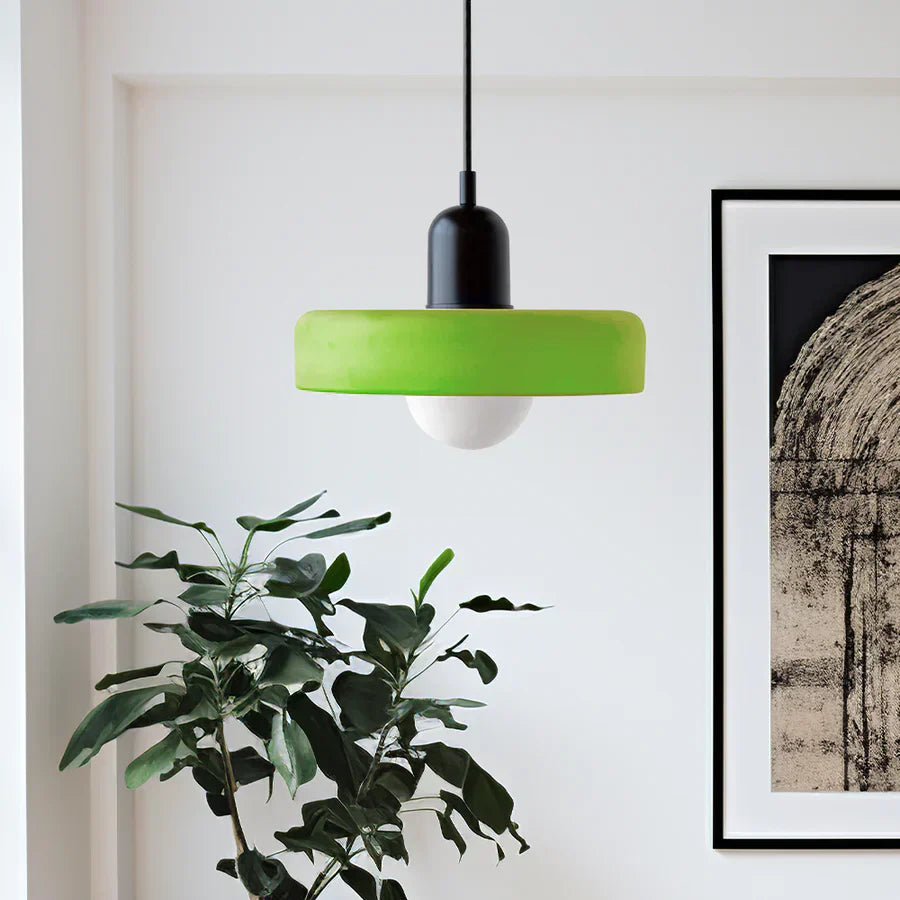 Moderne grüne Pendelleuchte mit schwarzem Sockel, hängend über Zimmerpflanze, minimalistisch.