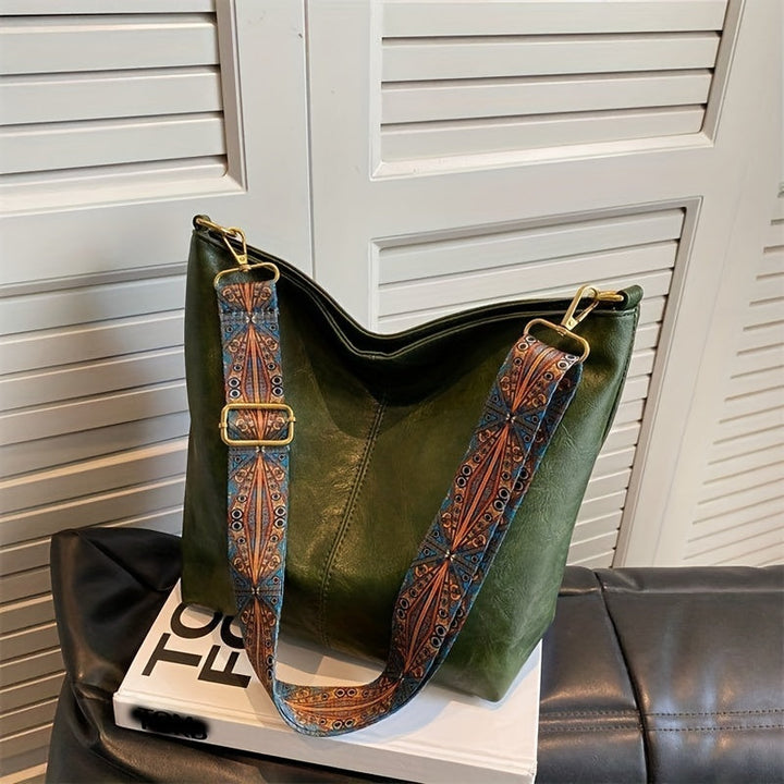 Grüne Ledertasche mit gemustertem Schultergurt auf schwarzem Sofa, stilvoll und modern.