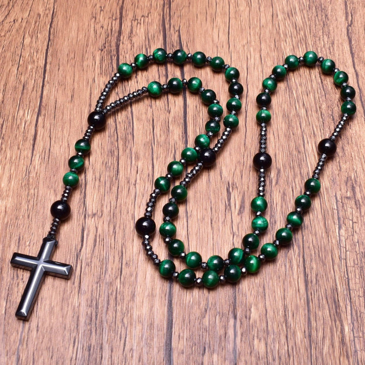 Grüne Rosenkranzkette mit schwarzem Kreuz, Holzperlen, religiöses Schmuckstück auf Holztisch.