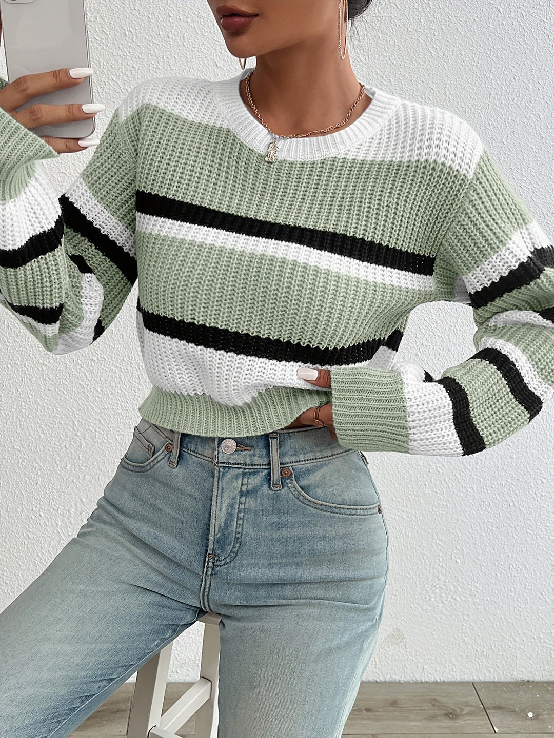 Frau in gestreiftem, grün-weiß-schwarzem Strickpullover und Jeans, modisch, lässig.