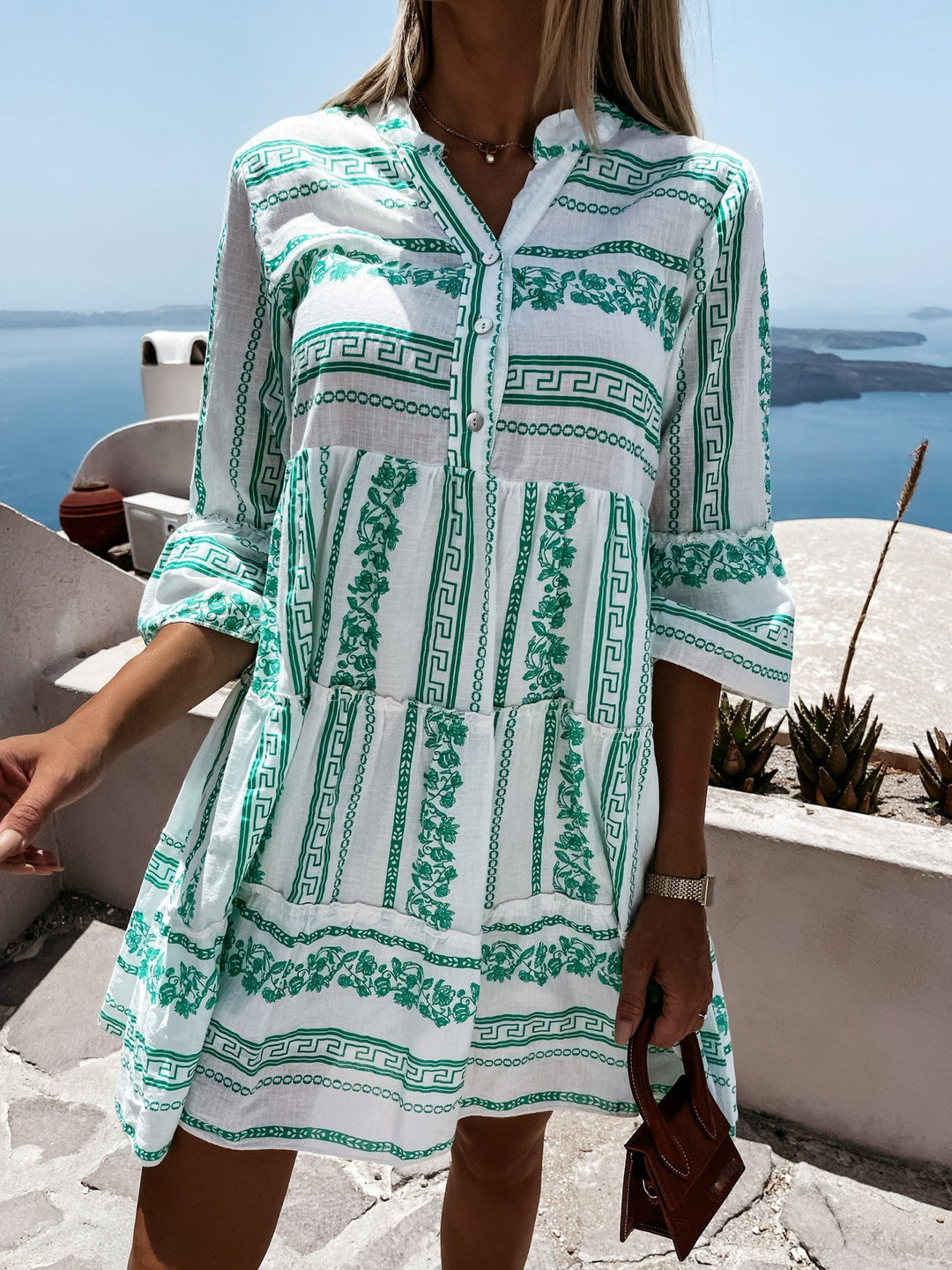 Frau in weißem und grünem Sommerkleid mit griechischem Muster, Meerblick im Hintergrund.