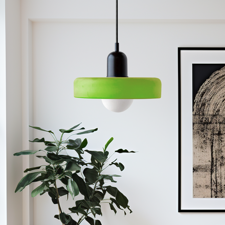 Grüne Hängelampe aus Glas, modernes Design, über Zimmerpflanze und Kunstwerk an weißer Wand.