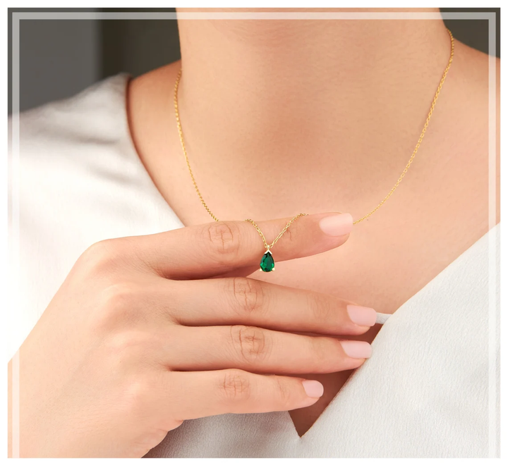 Frau mit goldener Halskette und grünem Edelstein-Anhänger, eleganter Schmuck, Nahaufnahme.