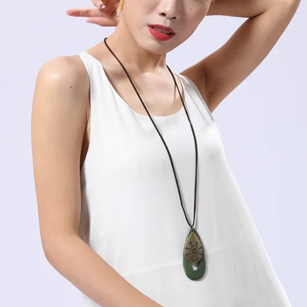 Frau mit weißem Kleid und grünem Anhänger-Halskette, modisches Accessoire, eleganter Schmuck.