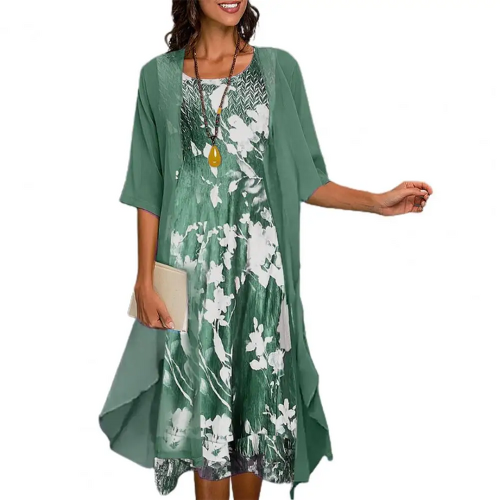 Frau in grünem Sommerkleid mit Blumenmuster und Halskette, hält eine Clutch.