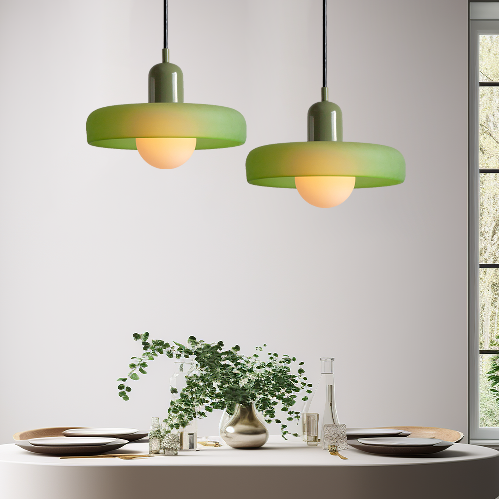 Zwei grüne Pendelleuchten über Esstisch mit Geschirr und Vase, modernes Innendesign.