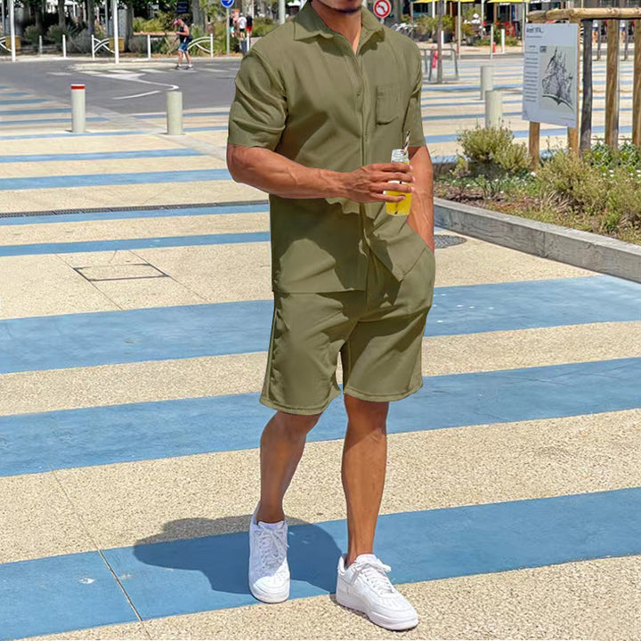 Mann in olivgrünem Kurzarm-Overall, hält Getränk, trägt weiße Sneaker, Sommermode.