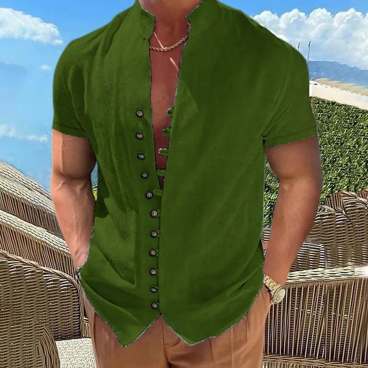 Mann in grünem Leinenhemd, kurzärmelig, mit Knopfleiste, Sommermode, vor Strandkulisse.