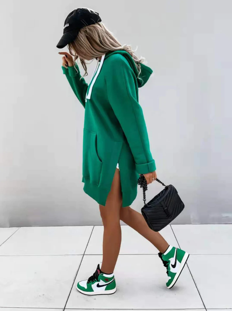 Frau in grünem Hoodie-Kleid, schwarze Mütze, Nike-Sneaker, schwarze Tasche, seitlich gehend.