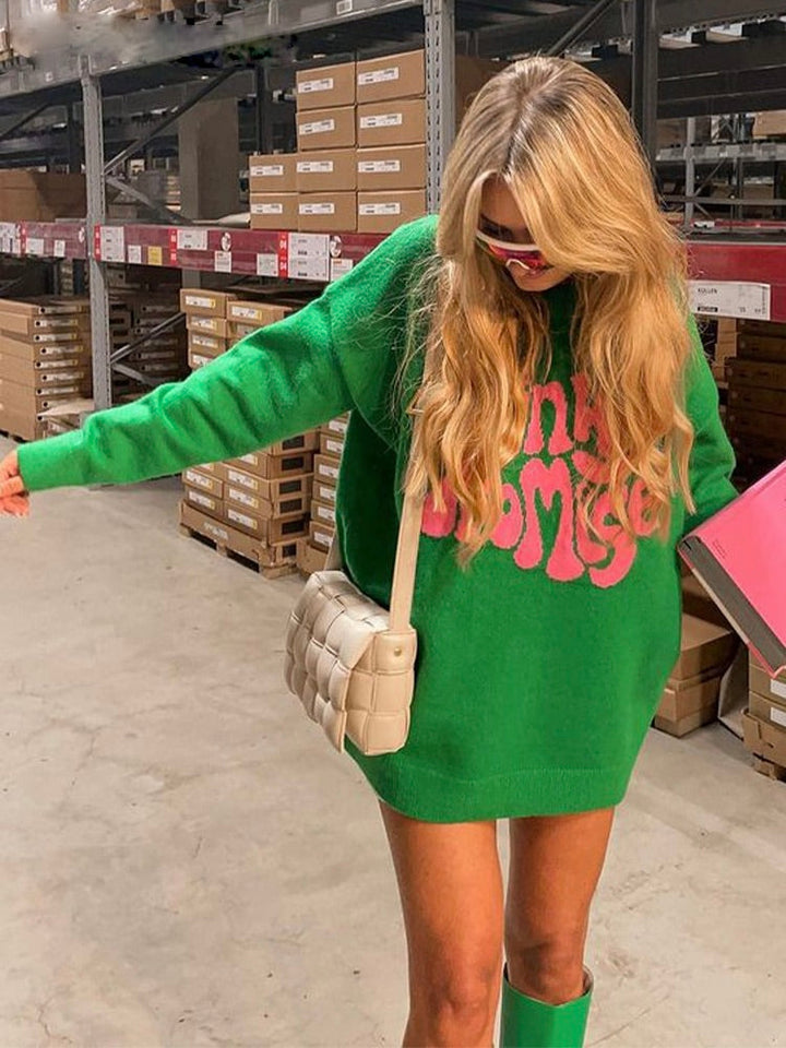 Frau in grünem Oversize-Pullover mit pinkem Schriftzug, weiße Umhängetasche, Lagerumgebung.