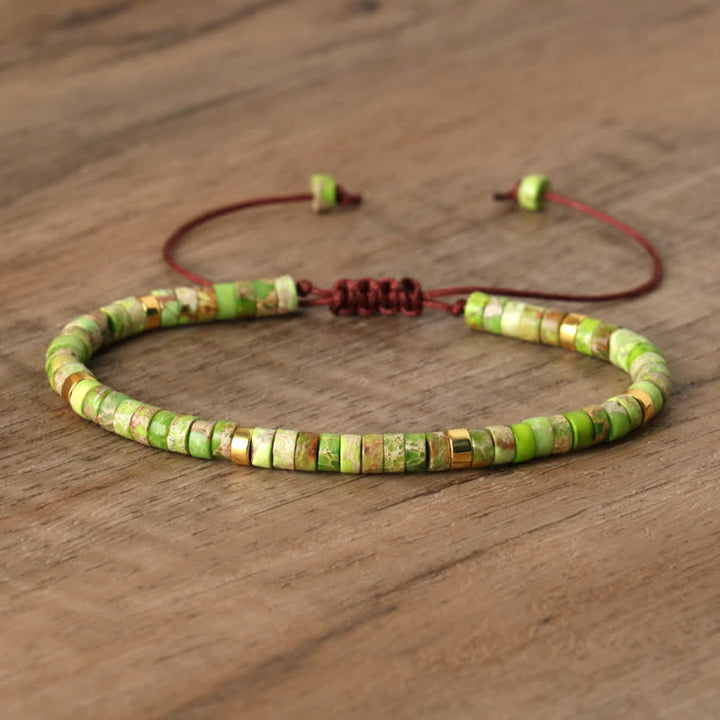 Grünes Perlenarmband aus Naturstein mit verstellbarem braunem Band auf Holzoberfläche.