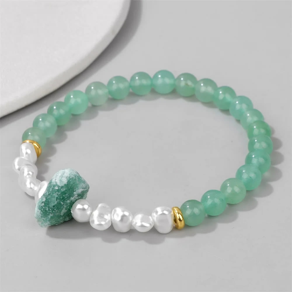 Grünes Aventurin-Perlenarmband mit weißen Perlen und goldenen Akzenten auf grauem Hintergrund.