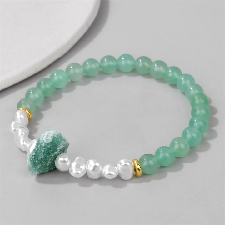 Grünes Aventurin-Perlenarmband mit weißen Perlen und goldenen Akzenten auf grauem Hintergrund.