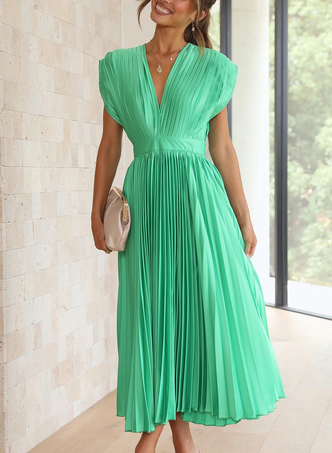 Frau in grünem, plissiertem Kleid, V-Ausschnitt, elegantes Design, Sommermode, Innenraum.