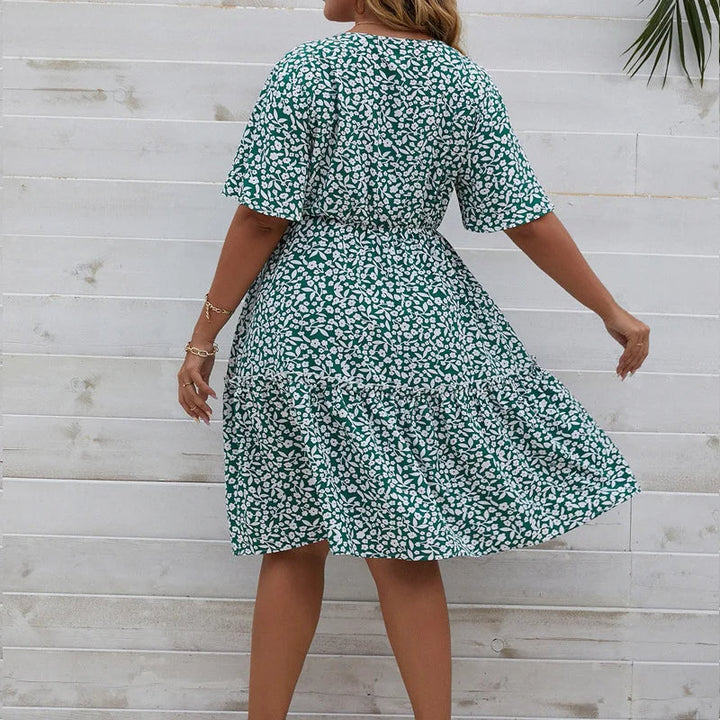 Frau in grünem Sommerkleid mit weißem Blumenmuster vor Holzwand.